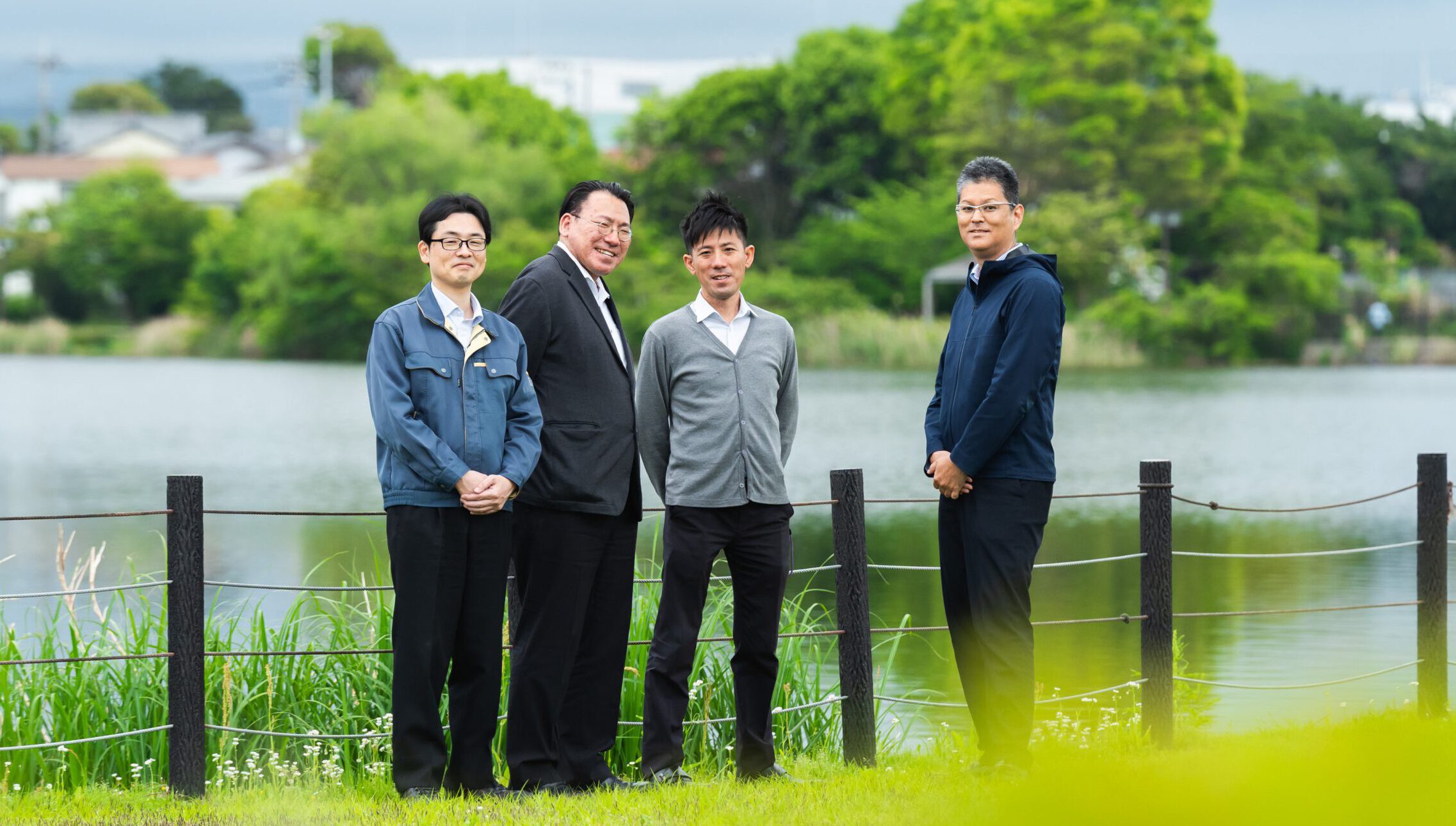 豊かな自然あふれる川をバックに立つアークの社員4名